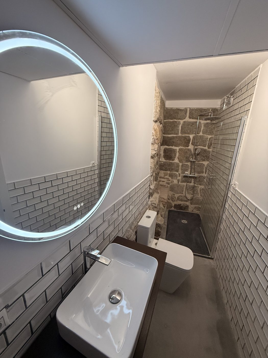 Baño con pared de piedra natural, microcemento y espejo LED